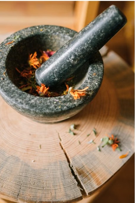 A stone mortar and pestle holding dried calendula petals on a wooden stump